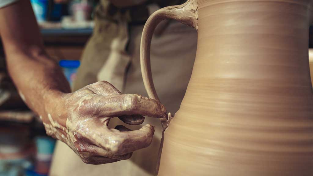 A potter adding a handle to a wheel-thrown jug.