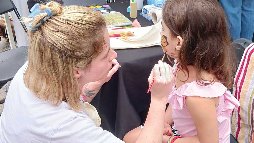 A child getting her face painted by an Art Center Volunteer