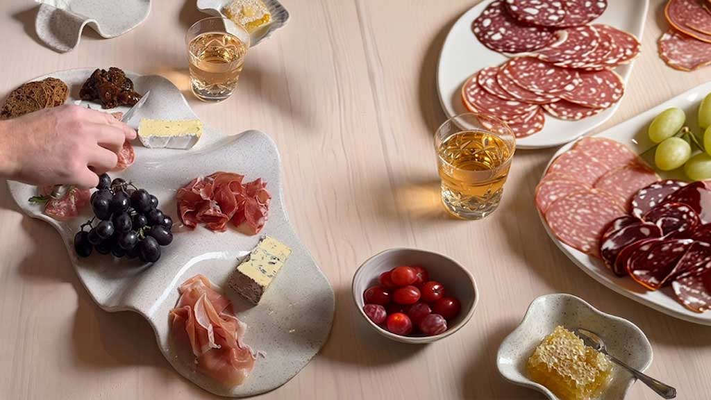A ceramic charcuterie set filed with cured meats, cheese and fruit.